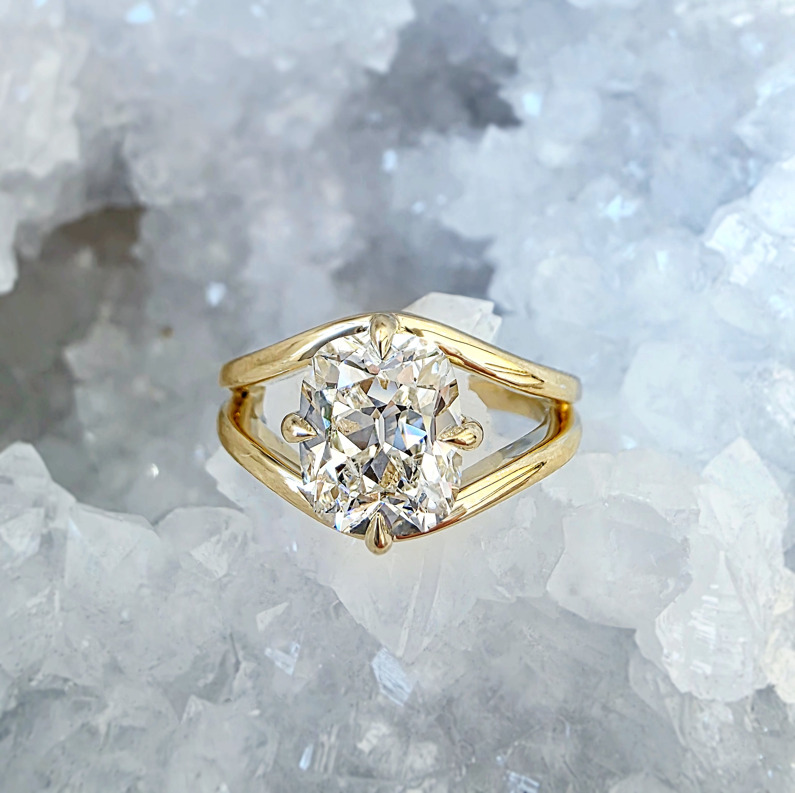 Oval diamond engagement ring in a sculptural yellow-gold setting, photographed on white crystal